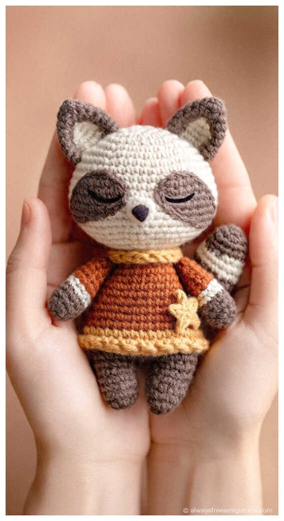 Small raccoon crochet doll wearing a brown sweater resting in cupped hands
