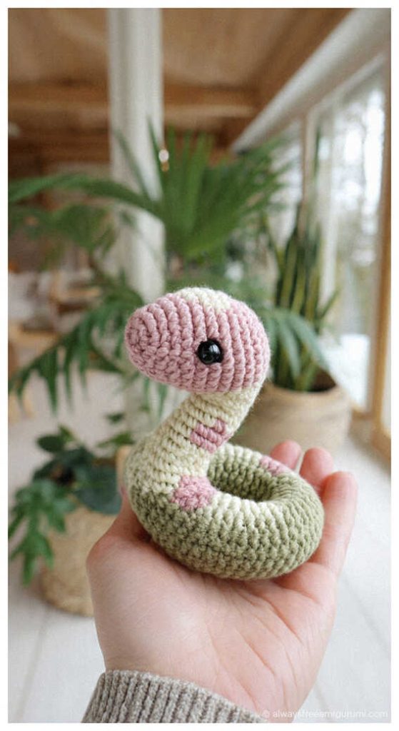 Cute pastel green and pink snake amigurumi coiled in hand, soft crochet snake toy idea for nursery decor