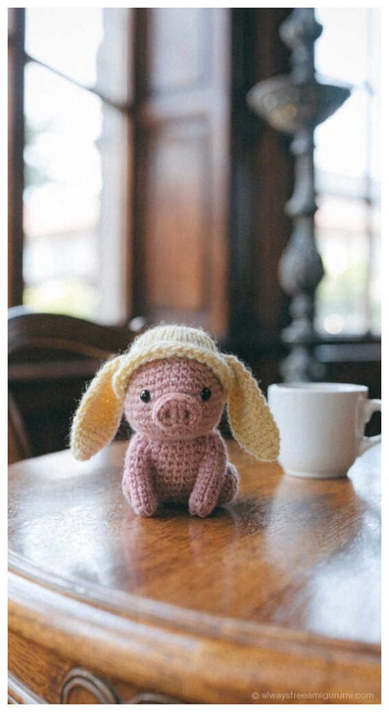 Small pig amigurumi with bunny ears sitting on table, cute crochet pig plush idea