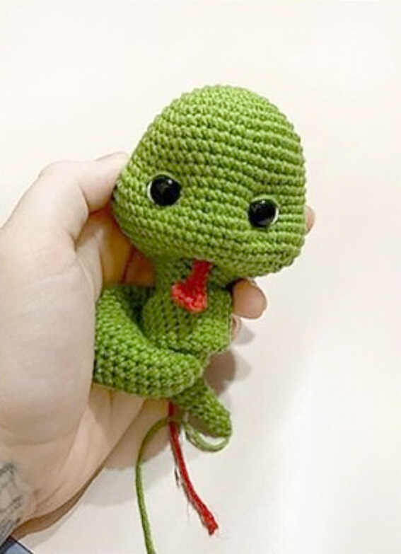 Green snake amigurumi with red tongue being attached during assembly